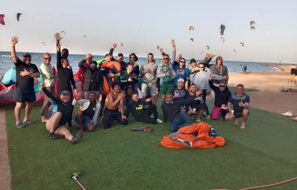 Group of kitesurfers and the Sultan Kite School team waving on the beach