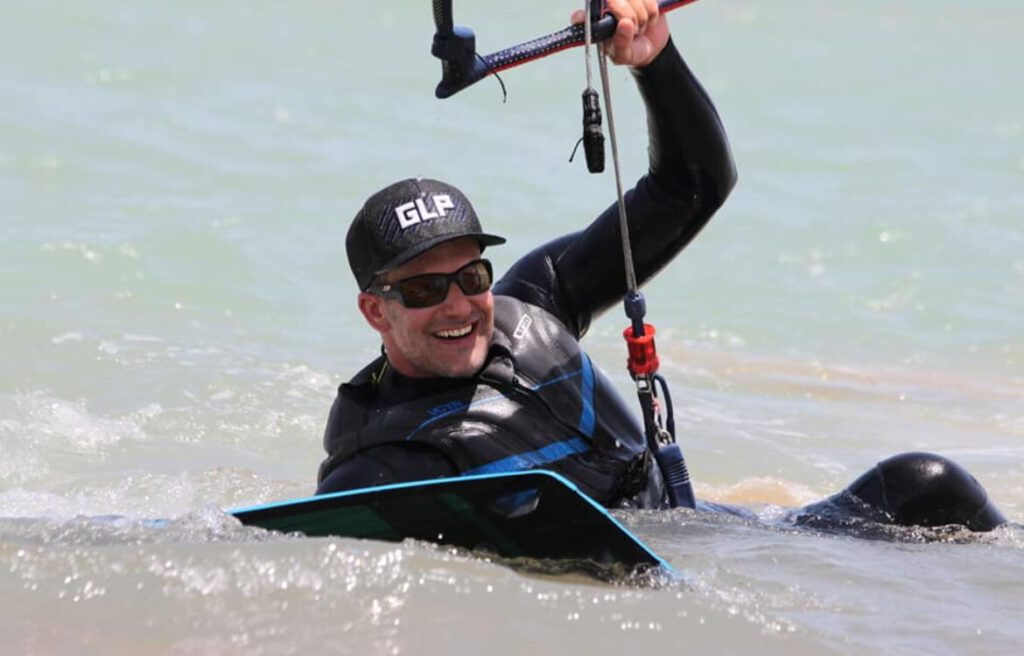 Smiling kitesurfer in a cap getting up on the board in the lagoon