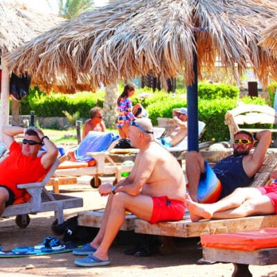 Riders relaxing under a palm-leaf parasol in the chill-out zone at the kite spot